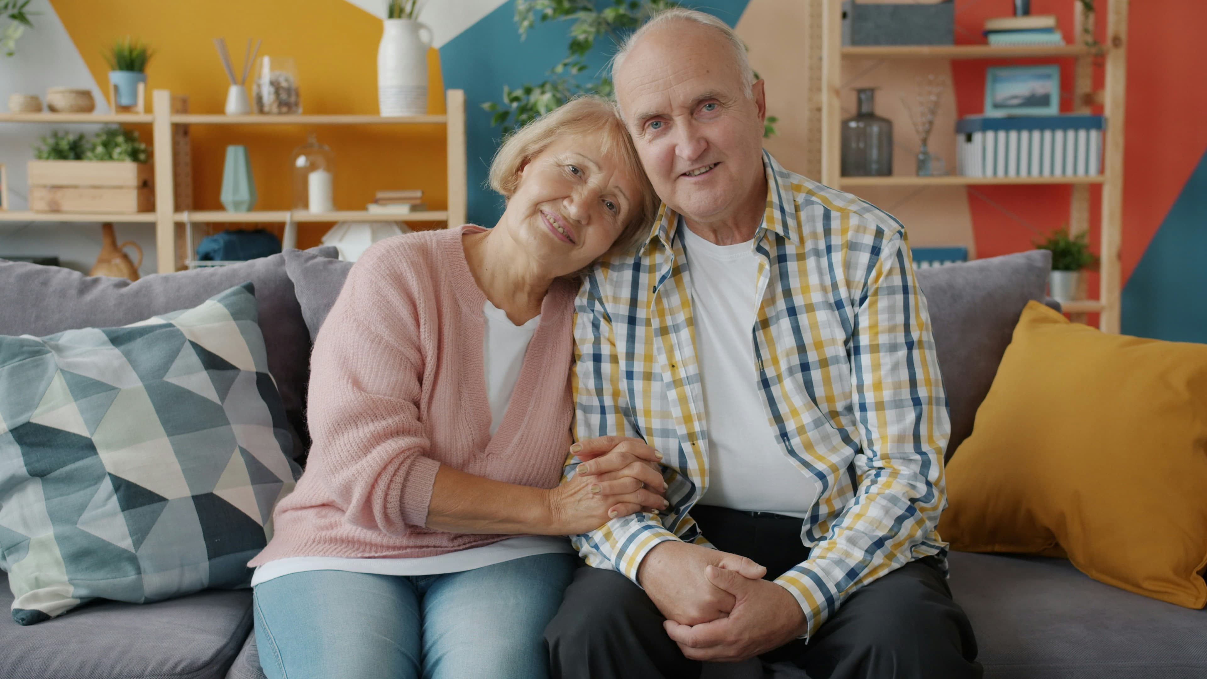 An older couple sitting together on a sofa at home, smiling