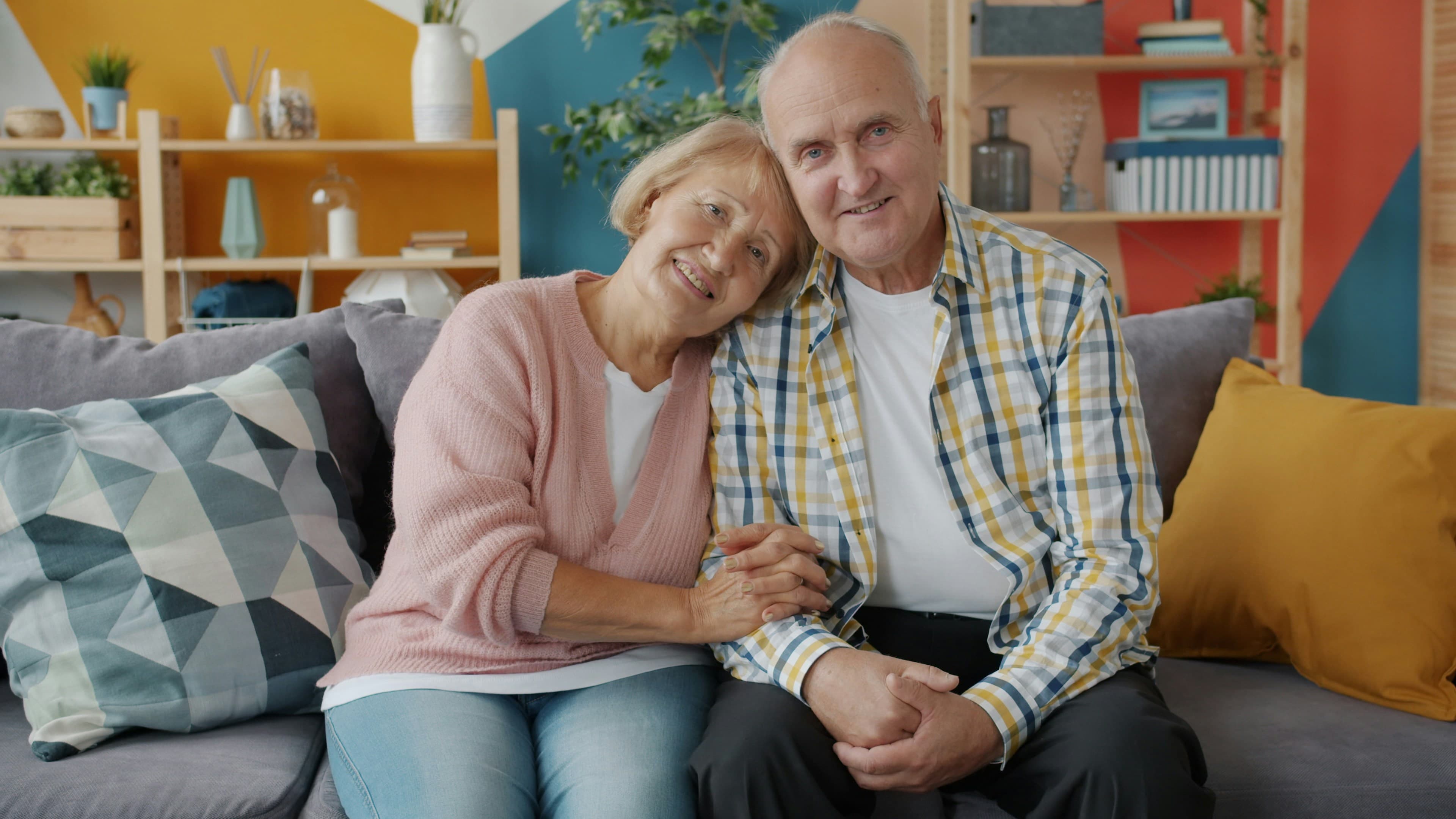An older couple sitting together on a sofa at home, holding hands
